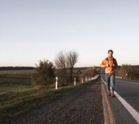 homem caminha em estrada, virado para nós, no meio de um campo