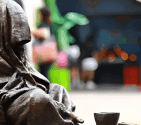 estátua de homem sentado no chão, a mendigar cabeça coberta, que olhado com atenção, se pode reconhecer como Jesus Cristo pelas chagas nas suas mãos