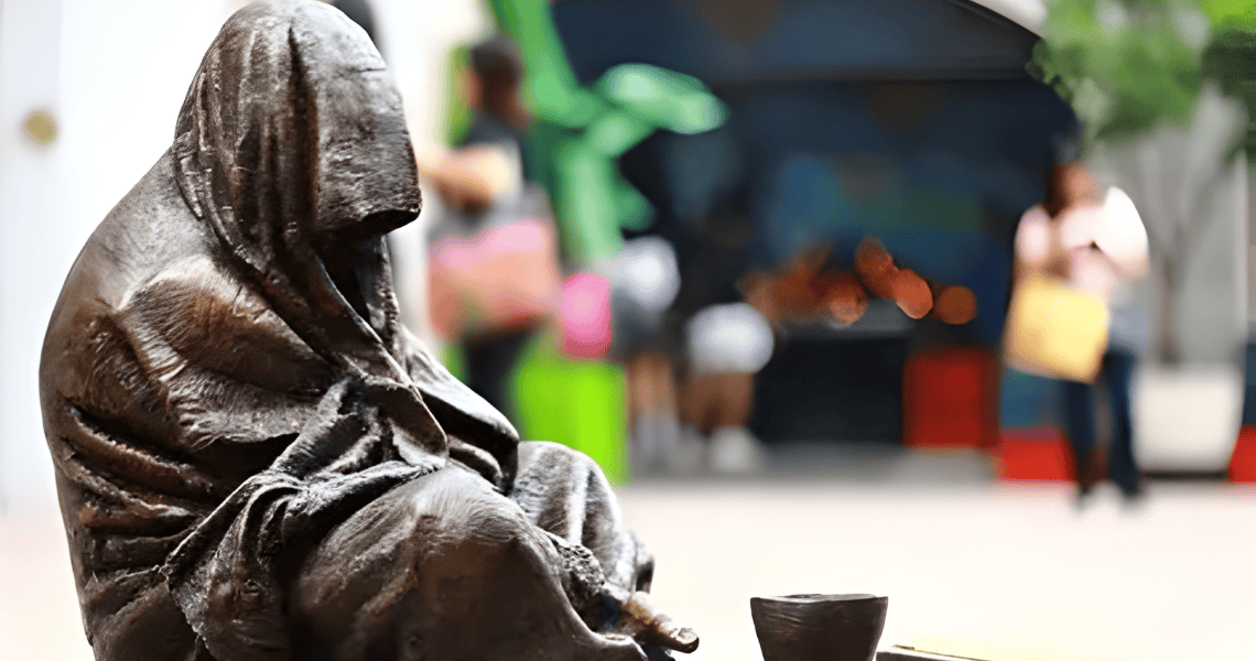 estátua de homem sentado no chão, a mendigar cabeça coberta, que olhado com atenção, se pode reconhecer como Jesus Cristo pelas chagas nas suas mãos