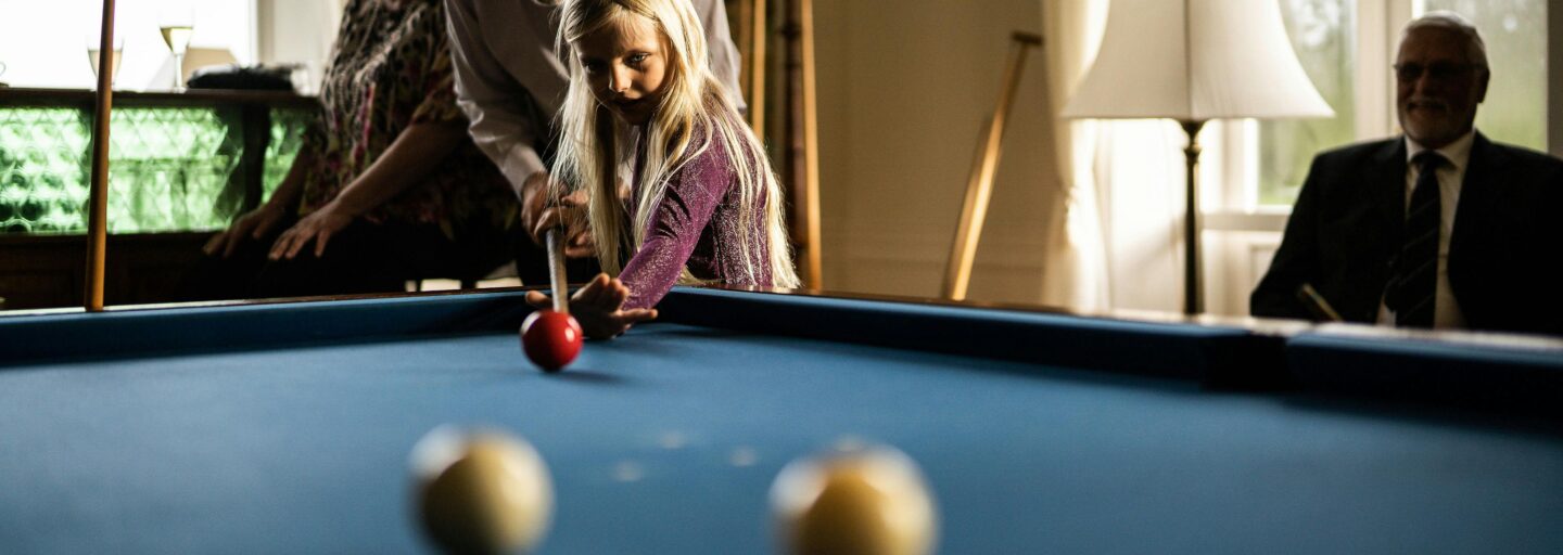 Avô ajuda a neta a segurar o taco num jogo de snooker.