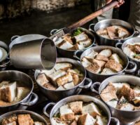 vários pequenos tachos seguidos, com pão dentro, e uma concha que deposita sopa em cada um