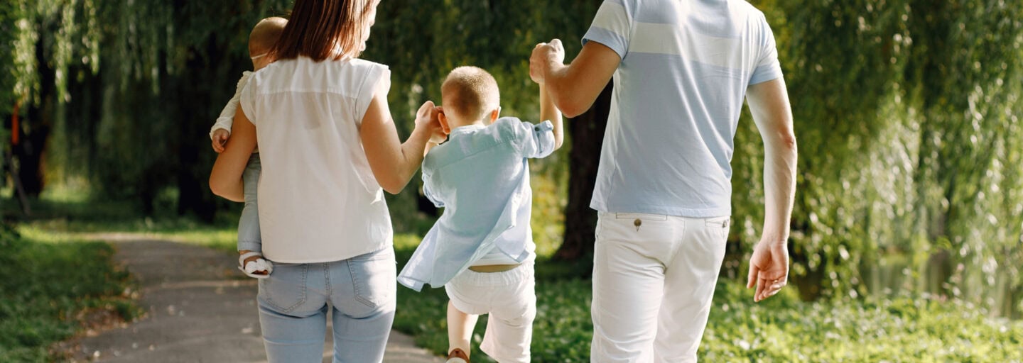 mãe e pai passeiam num parque solarengo enquanto seguram pelas mãos um filho que salta