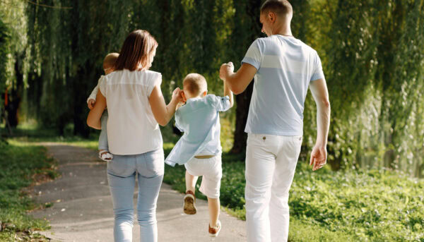 mãe e pai passeiam num parque solarengo enquanto seguram pelas mãos um filho que salta