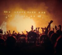 vista desde a multidão de um concerto, com palco cheio de luz entrevisto por braços no ar
