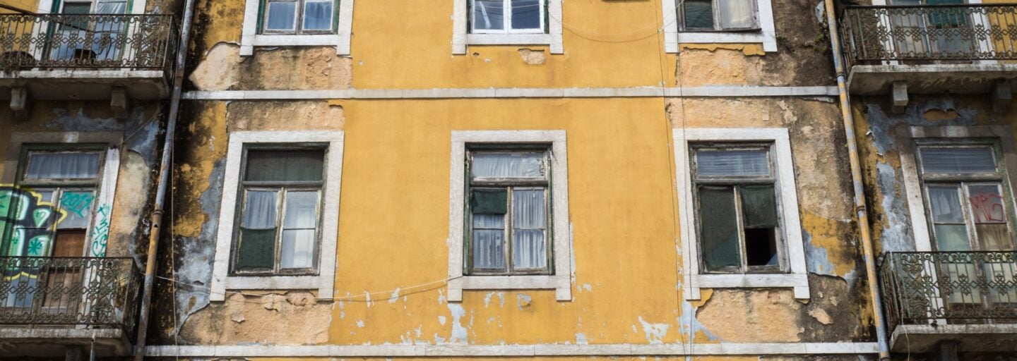 foto vertical de um edifício antigo, de cor amarela, com algumas janelas partidas