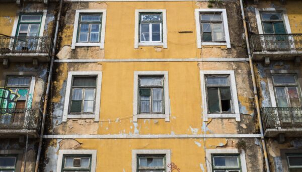 foto vertical de um edifício antigo, de cor amarela, com algumas janelas partidas