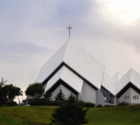 igreja moderna, branca, de telhados em planos inclinados simétricos como livro aberto pousado sobre uma mesa, num horizonte ao pôr do sol