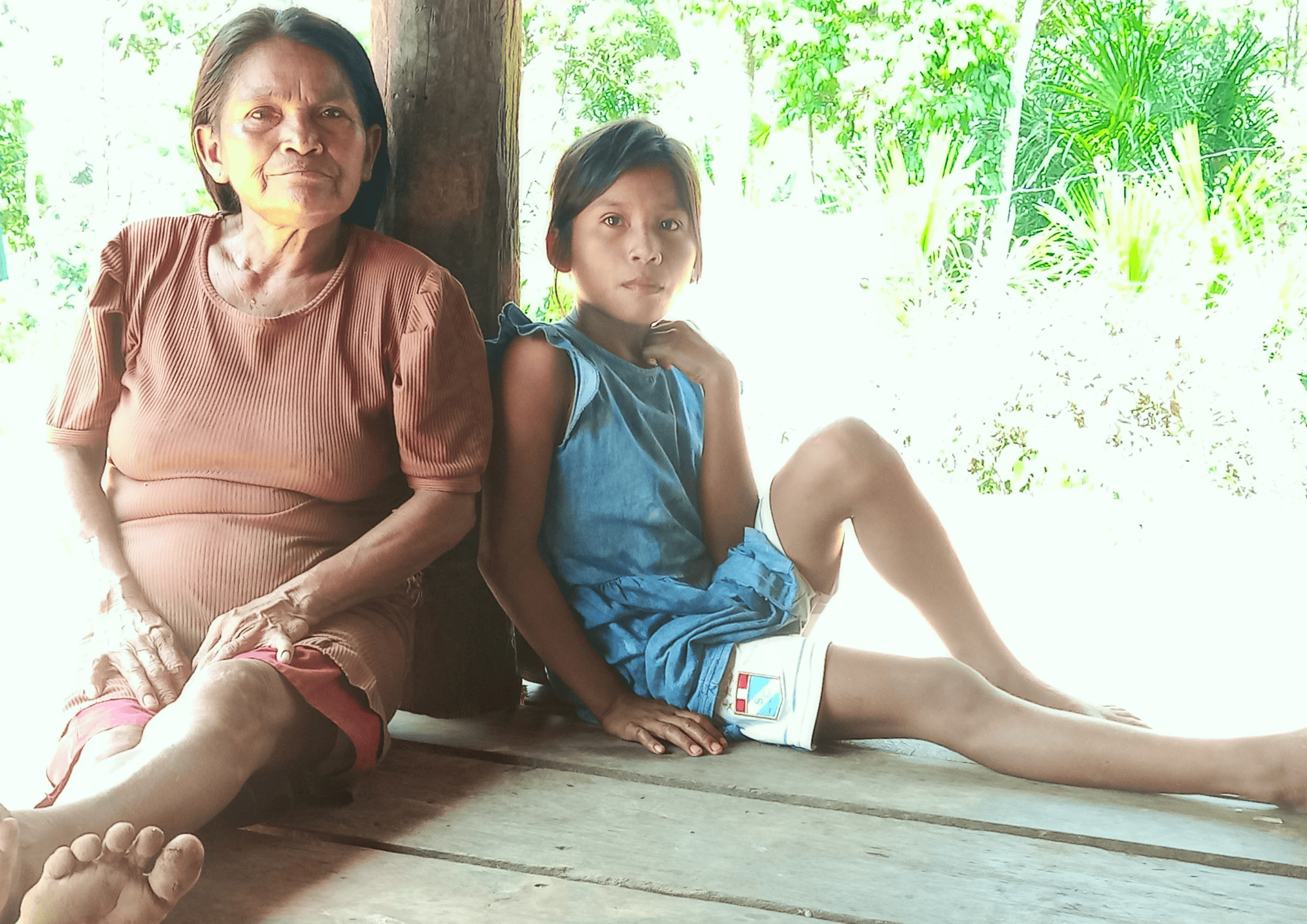 Una mujer y un niño indígenas se sientan en una choza de madera, mirando la fotografía.