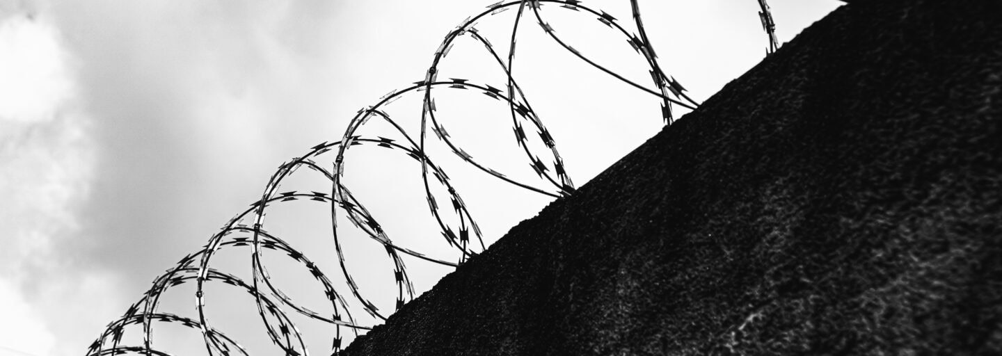 fotografia a preto e branco de muro coroado de serpentina de arame farpado