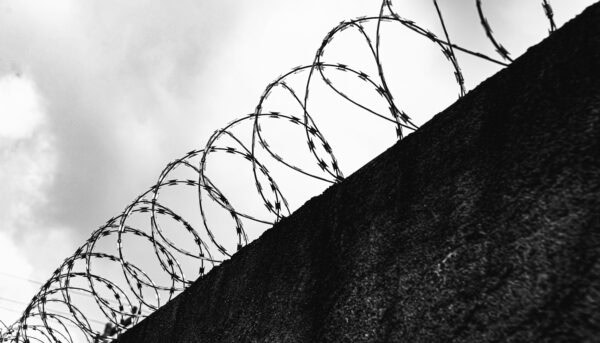 fotografia a preto e branco de muro coroado de serpentina de arame farpado