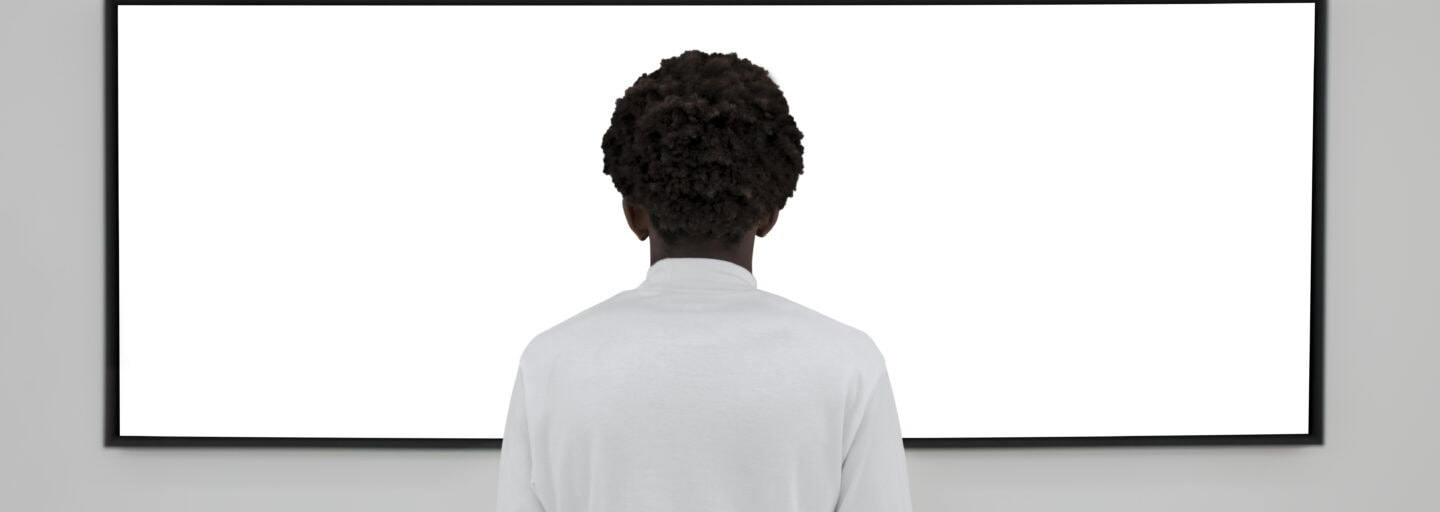 homem diante de ecrã de parede, em branco, de costas para o espectador, permanece absorto