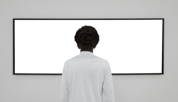 homem diante de ecrã de parede, em branco, de costas para o espectador, permanece absorto
