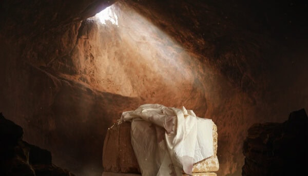 gruta escavada na rocha, com pedra no centro coberta por um lençol enxovalhado, iluminados por um frincha circular no superior da gruta