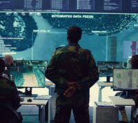 Em ambiente escuro cuja única fonte de luz é um azul dos ecrãs, oficial do Exército a analisar imagens de vigilância por satélite num ecrã gigante para fins de reconhecimento, recolhendo informações para garantir a segurança nacional.
