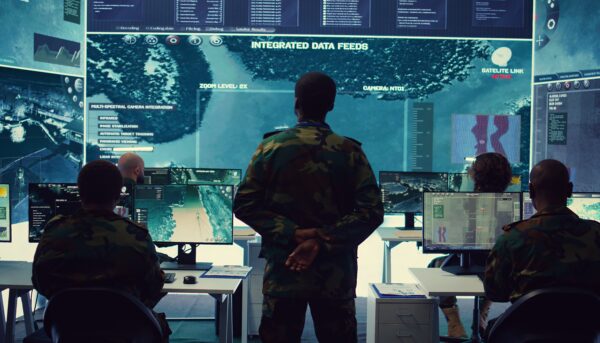 Em ambiente escuro cuja única fonte de luz é um azul dos ecrãs, oficial do Exército a analisar imagens de vigilância por satélite num ecrã gigante para fins de reconhecimento, recolhendo informações para garantir a segurança nacional.