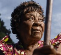 mulher negra olha com esperança para o horizonte, tendo a marca do passar dos anos marcada na cara