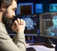 Num ambiente de luz de ecrã azul, um jovem homem com barba, programador de software, observa, incrédulo, a inteligência artificial a ganhar forma humanoide no ecrã sem qualquer comando ou aviso, e a dar sinais de consciência.