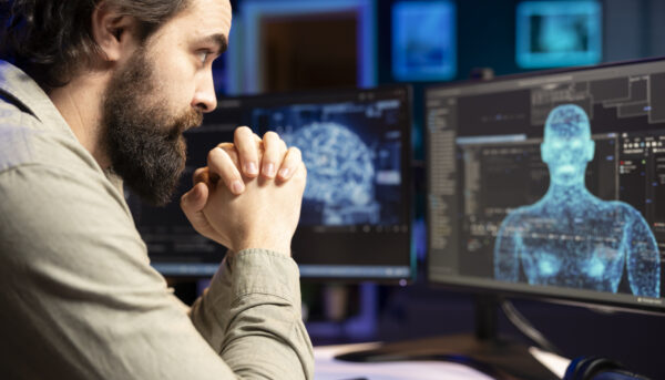 Num ambiente de luz de ecrã azul, um jovem homem com barba, programador de software, observa, incrédulo, a inteligência artificial a ganhar forma humanoide no ecrã sem qualquer comando ou aviso, e a dar sinais de consciência.