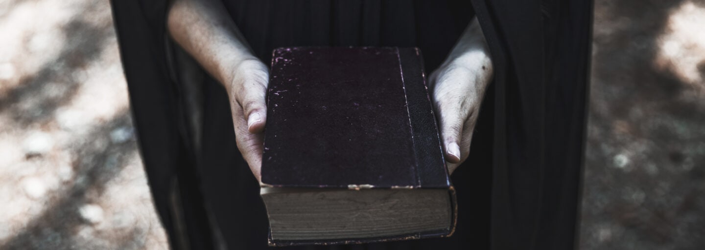 “Uma mulher vestida de preto segura um livro antigo nas mãos.”