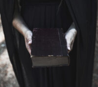 “Uma mulher vestida de preto segura um livro antigo nas mãos.”