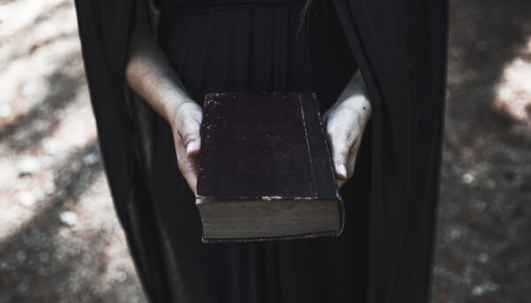 “Uma mulher vestida de preto segura um livro antigo nas mãos.”
