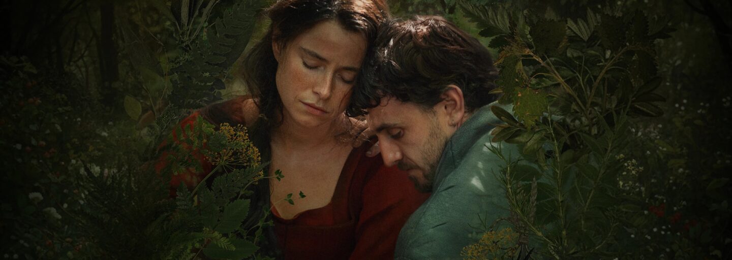 Duas pessoas sentam‑se juntas numa floresta verde e luminosa. Uma veste vermelho, a outra verde. Estão encostadas, de olhos fechados, num momento de calma e intimidade, envolvidas pela luz suave que atravessa as folhas.